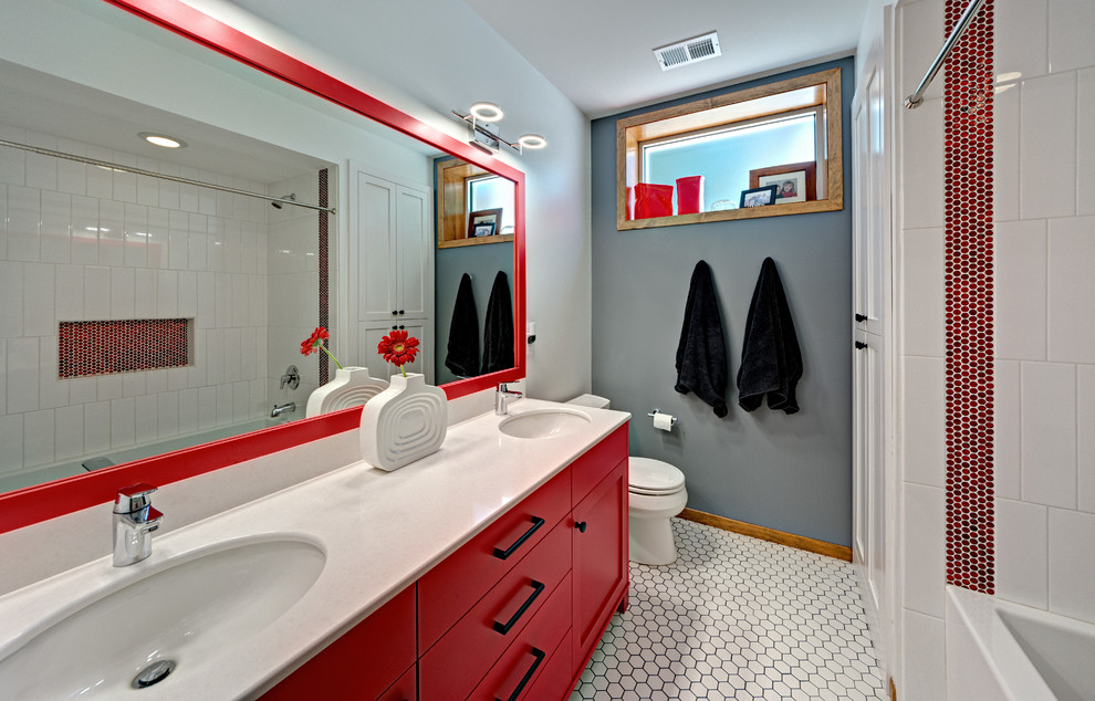 Photo of a mid-sized contemporary kids bathroom in Minneapolis with recessed-panel cabinets, red cabinets, an alcove tub, a shower/bathtub combo, a two-piece toilet, white tile, ceramic tile, multi-coloured walls, ceramic floors, an undermount sink and engineered quartz benchtops.