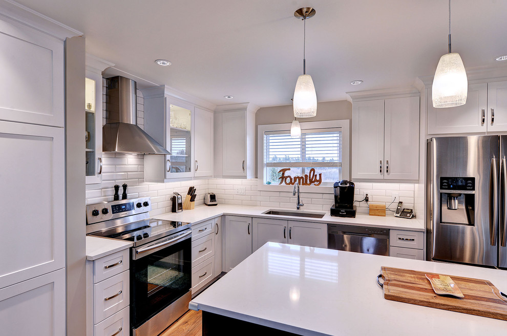 Inspiration for a transitional dark wood floor and brown floor enclosed kitchen remodel with a single-bowl sink, shaker cabinets, white cabinets, quartzite countertops, white backsplash, subway tile backsplash, stainless steel appliances and an island