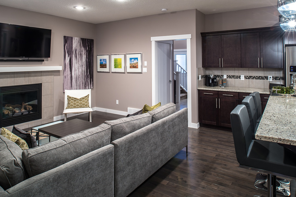 Inspiration for a modern open concept family room in Edmonton with a game room, grey walls, dark hardwood floors, a standard fireplace, a tile fireplace surround and a wall-mounted tv.