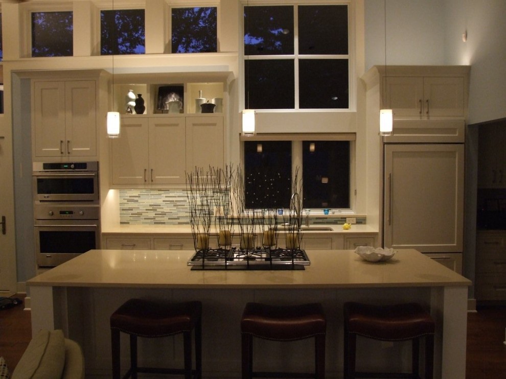 Example of a mid-sized transitional l-shaped medium tone wood floor kitchen design in Chicago with an undermount sink, green backsplash, glass tile backsplash, paneled appliances, shaker cabinets, white cabinets, solid surface countertops and an island