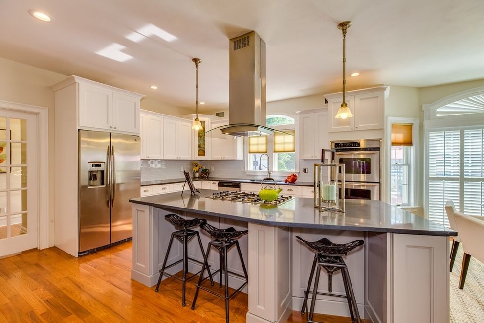 Kitchen - large transitional l-shaped medium tone wood floor kitchen idea with an undermount sink, recessed-panel cabinets, white cabinets, quartz countertops, white backsplash, glass tile backsplash, stainless steel appliances and an island