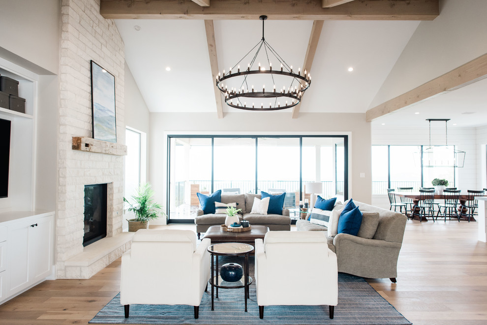 This is an example of a large transitional open concept family room in Austin with grey walls, light hardwood floors, a standard fireplace, a stone fireplace surround, a wall-mounted tv and brown floor.