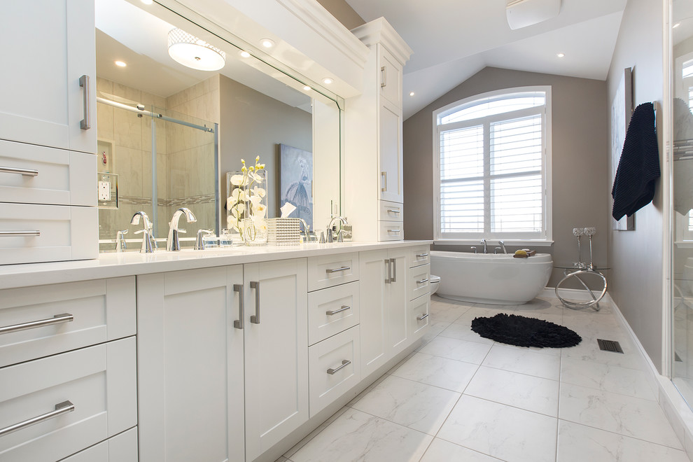 Inspiration for a large transitional master bathroom in Toronto with shaker cabinets, white cabinets, a freestanding tub, a double shower, a one-piece toilet, grey walls, an undermount sink, engineered quartz benchtops and light hardwood floors.
