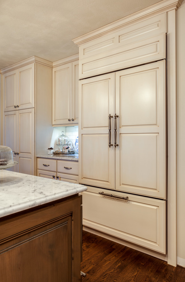 デンバーにある高級な広いシャビーシック調のおしゃれなキッチン (エプロンフロントシンク、レイズドパネル扉のキャビネット、白いキャビネット、大理石カウンター、白いキッチンパネル、サブウェイタイルのキッチンパネル、パネルと同色の調理設備、無垢フローリング、茶色い床、白いキッチンカウンター) の写真