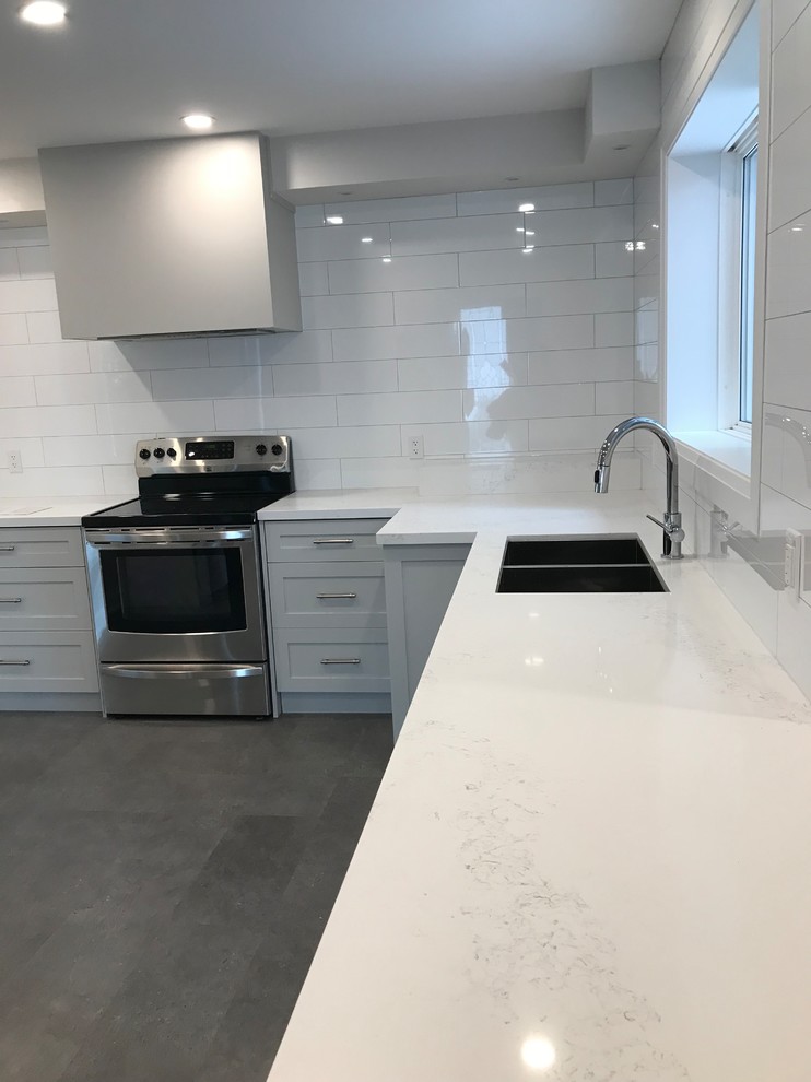 Inspiration for a mid-sized transitional separate kitchen in Toronto with an undermount sink, shaker cabinets, grey cabinets, quartz benchtops, white splashback, subway tile splashback, stainless steel appliances, porcelain floors, with island, brown floor and white benchtop.