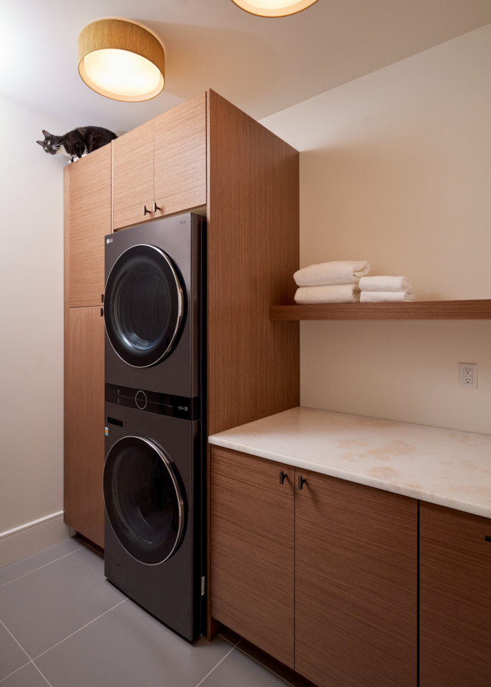 Design ideas for a large modern single-wall dedicated laundry room in Richmond with flat-panel cabinets, medium wood cabinets, marble benchtops, beige walls, ceramic floors, a stacked washer and dryer, grey floor and beige benchtop.