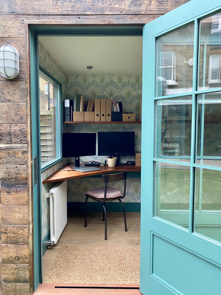 Diseño de despacho rural pequeño sin chimenea con paredes azules, suelo de madera clara, escritorio empotrado, suelo beige y papel pintado