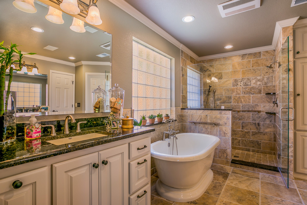 Large transitional master beige tile and stone tile travertine floor freestanding bathtub photo in Austin with raised-panel cabinets, gray cabinets, a two-piece toilet, gray walls, an undermount sink and granite countertops