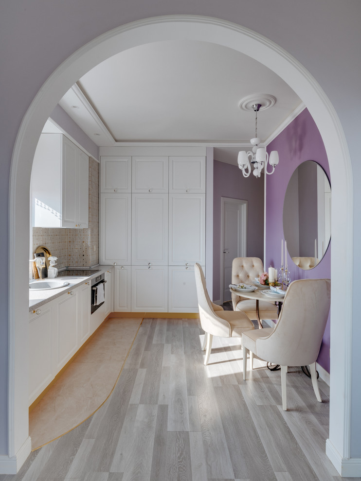 Design ideas for a transitional eat-in kitchen in Saint Petersburg with recessed-panel cabinets, white cabinets, beige splashback, light hardwood floors and grey benchtop.