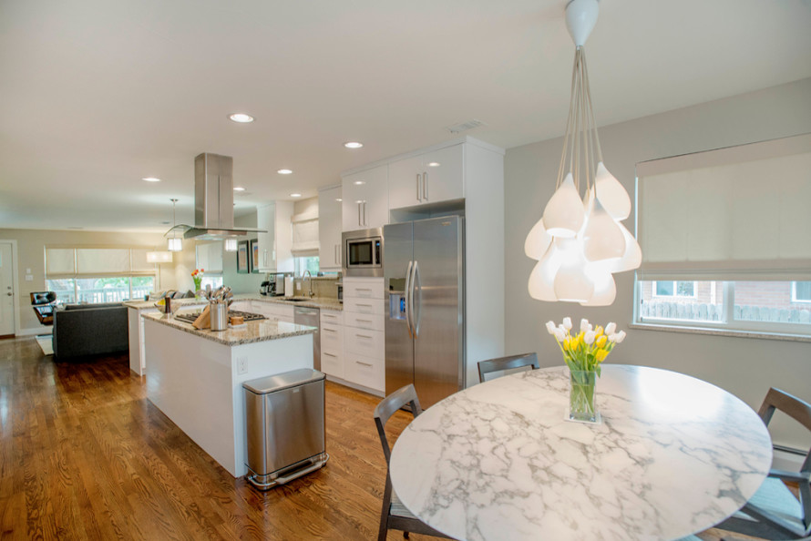 Example of a mid-sized transitional l-shaped light wood floor eat-in kitchen design in Denver with flat-panel cabinets, white cabinets, granite countertops, beige backsplash, subway tile backsplash, stainless steel appliances and an island