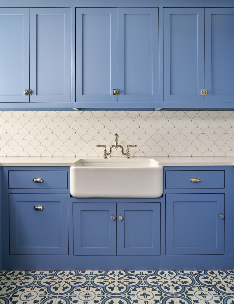 Inspiration for a mid-sized transitional l-shaped dedicated laundry room in Dallas with a farmhouse sink, shaker cabinets, blue cabinets, white walls, blue floor, white benchtop, solid surface benchtops and ceramic floors.
