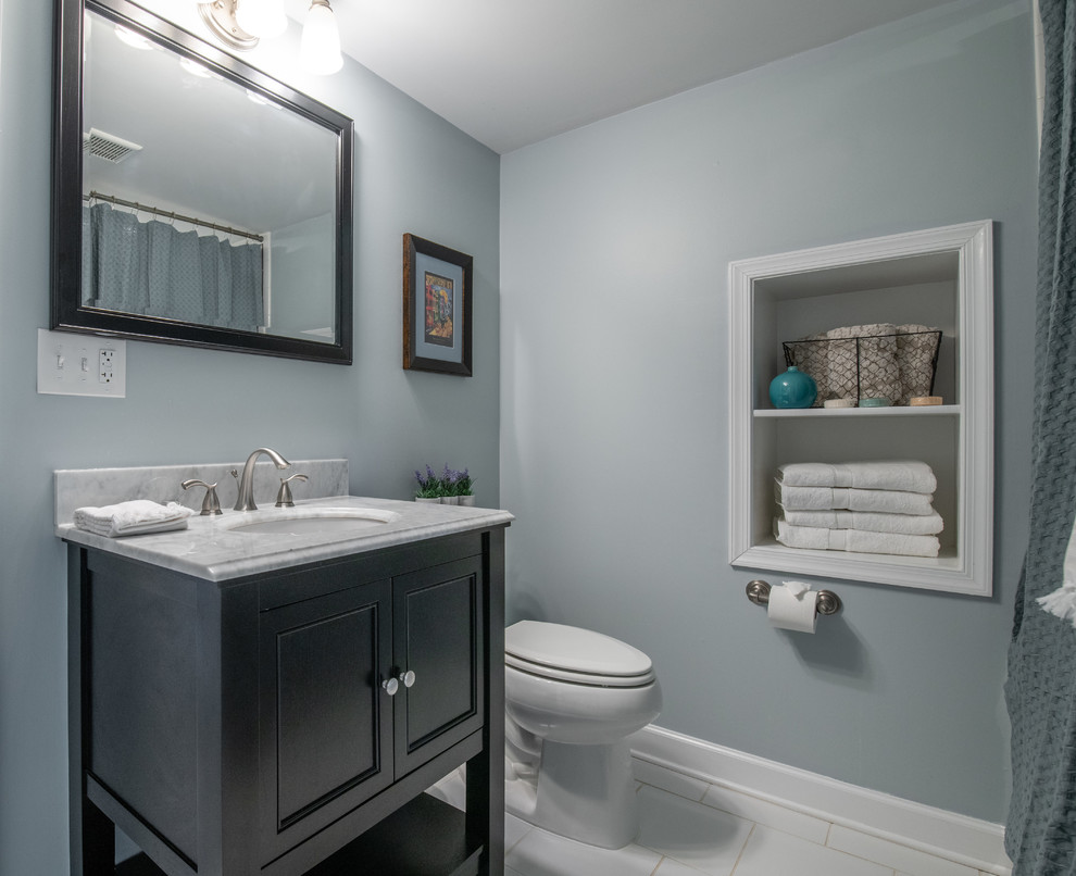 This is an example of a mid-sized traditional bathroom in DC Metro with furniture-like cabinets, black cabinets, an alcove shower, a two-piece toilet, white tile, subway tile, blue walls, ceramic floors, an undermount sink, white floor, a shower curtain, multi-coloured benchtops, a drop-in tub and marble benchtops.