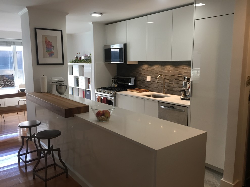 Inspiration for a small contemporary galley open plan kitchen in New York with a single-bowl sink, flat-panel cabinets, white cabinets, solid surface benchtops, black splashback, stone tile splashback, stainless steel appliances, porcelain floors, a peninsula, grey floor and white benchtop.
