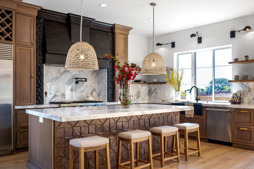 Photo of a mediterranean l-shaped open plan kitchen in San Diego with a farmhouse sink, medium wood cabinets, granite benchtops, stainless steel appliances, light hardwood floors, with island and white benchtop.