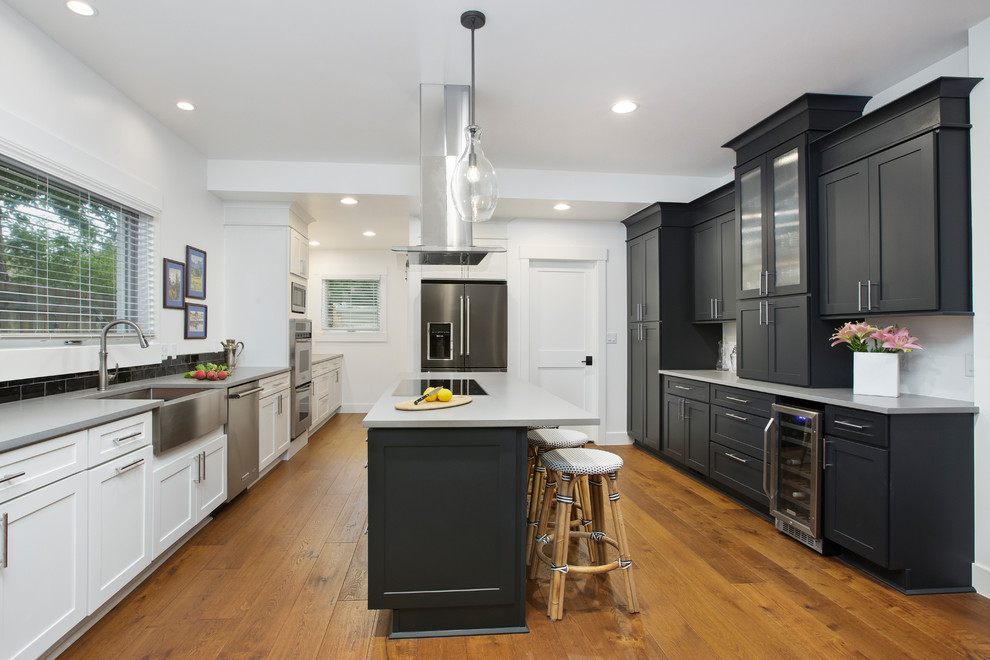 Inspiration for a country u-shaped kitchen in Denver with a farmhouse sink, shaker cabinets, black cabinets, black splashback, subway tile splashback, medium hardwood floors, with island, brown floor and grey benchtop.