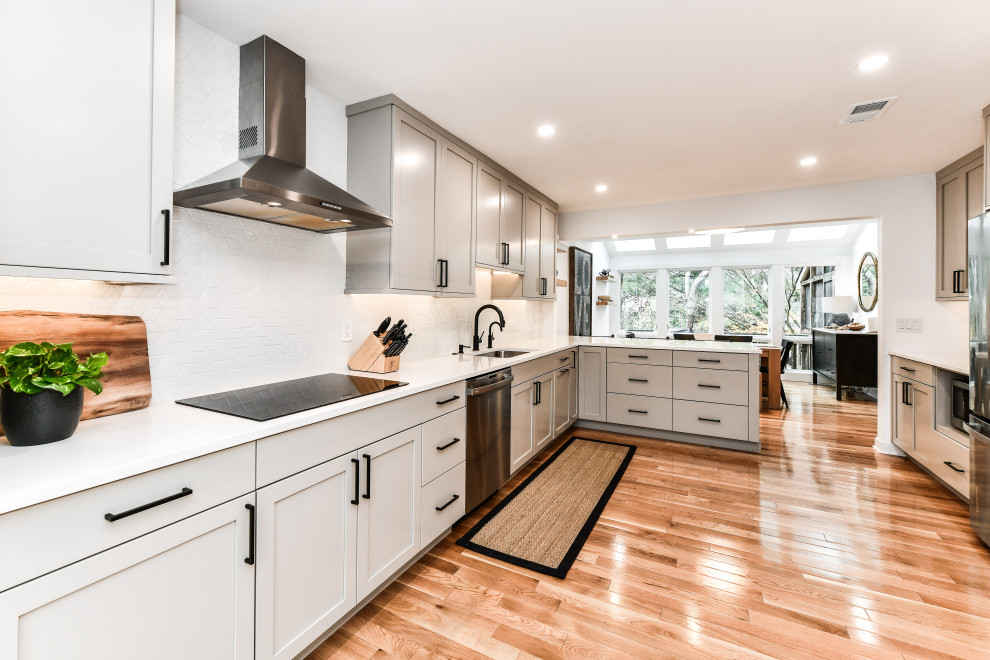Design ideas for a mid-sized transitional l-shaped eat-in kitchen in DC Metro with a single-bowl sink, shaker cabinets, beige cabinets, quartz benchtops, white splashback, ceramic splashback, black appliances, light hardwood floors, a peninsula and white benchtop.