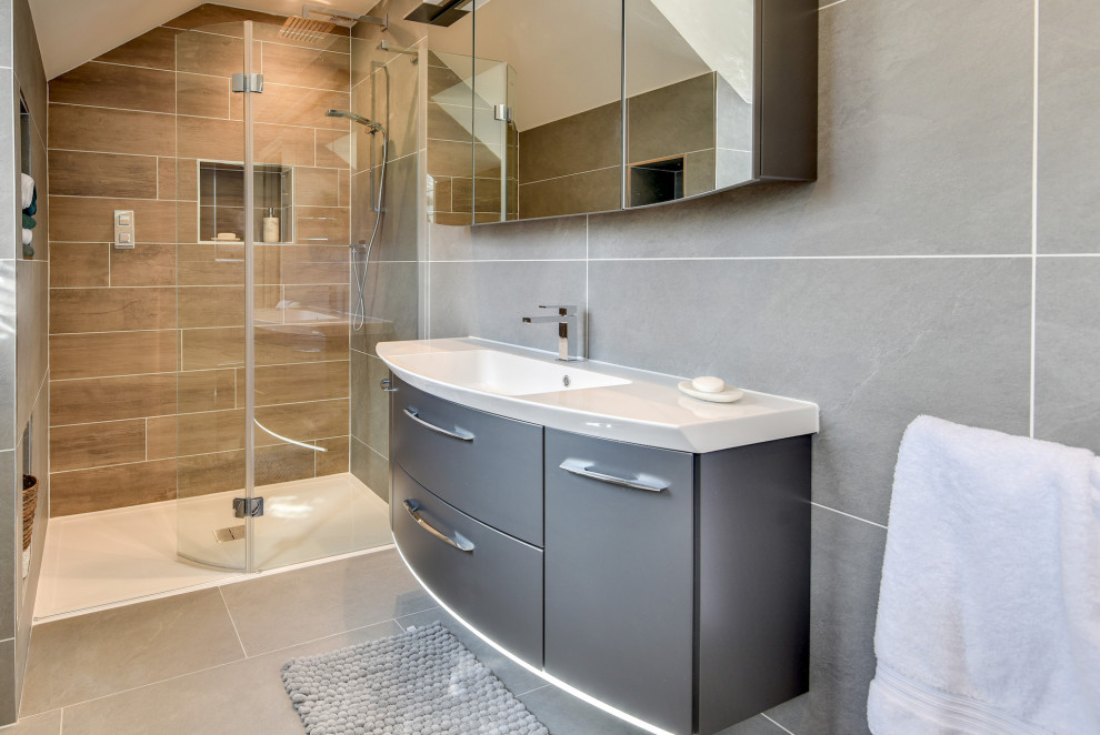 Стильный дизайн: большая главная, серо-белая ванная комната: освещение в стиле модернизм с плоскими фасадами, серыми фасадами, отдельно стоящей ванной, открытым душем, унитазом-моноблоком, серой плиткой, керамической плиткой, серыми стенами, полом из керамической плитки, накладной раковиной, стеклянной столешницей, серым полом, открытым душем, белой столешницей, тумбой под одну раковину и подвесной тумбой - последний тренд