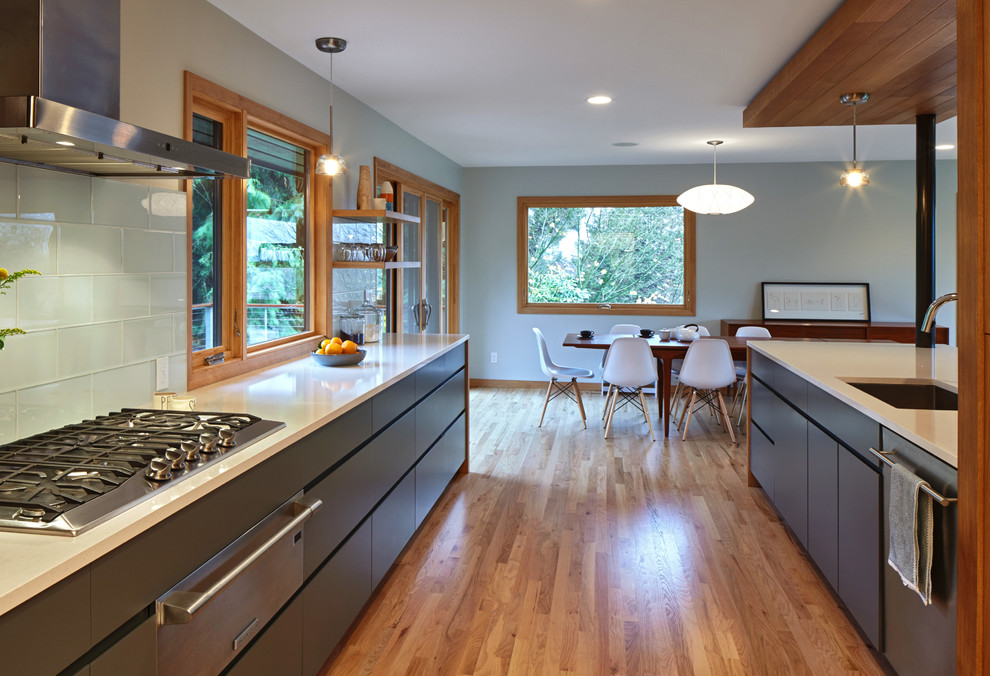 Photo of a contemporary galley eat-in kitchen in Portland with a drop-in sink, flat-panel cabinets, grey cabinets, quartz benchtops, white splashback, glass tile splashback, stainless steel appliances, medium hardwood floors and a peninsula.