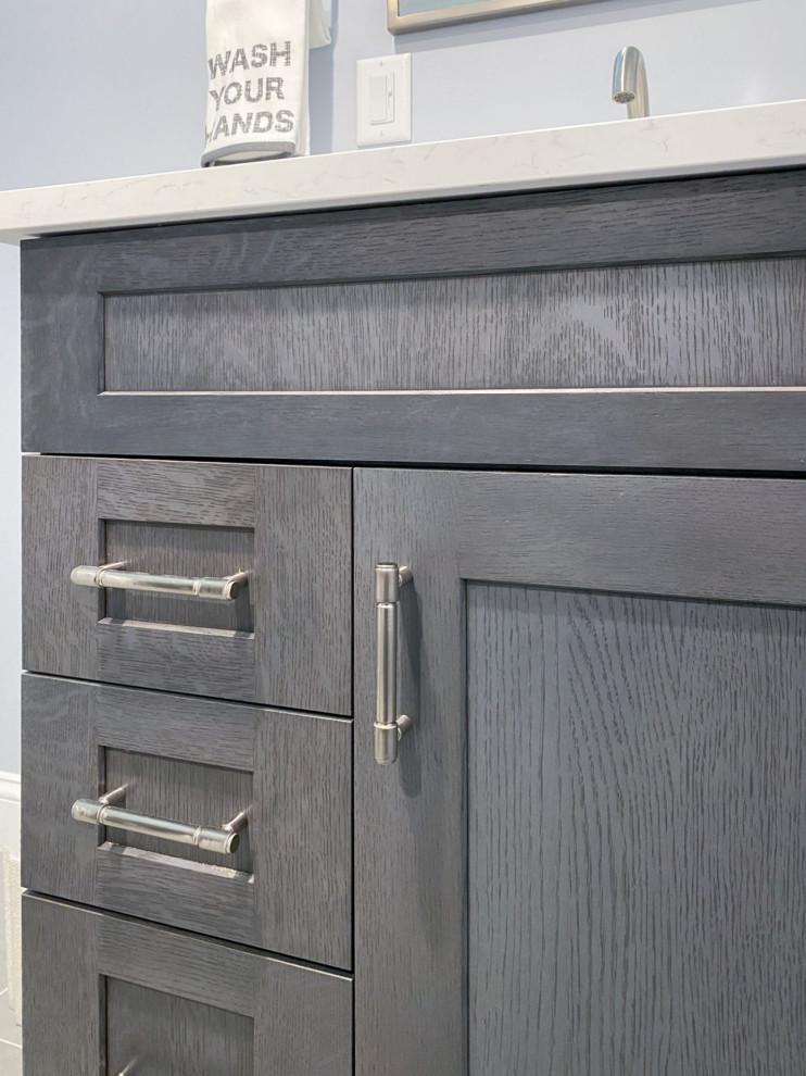 Example of a transitional white tile and ceramic tile porcelain tile, gray floor and single-sink corner shower design in Boston with shaker cabinets, gray cabinets, a one-piece toilet, gray walls, an undermount sink, quartz countertops, a hinged shower door, white countertops and a built-in vanity