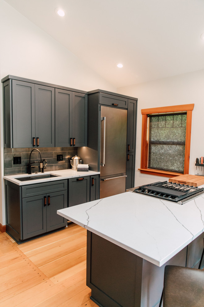 Small contemporary u-shaped open plan kitchen in Seattle with an undermount sink, shaker cabinets, grey cabinets, quartz benchtops, black splashback, porcelain splashback, stainless steel appliances, medium hardwood floors, a peninsula, brown floor, white benchtop and vaulted.