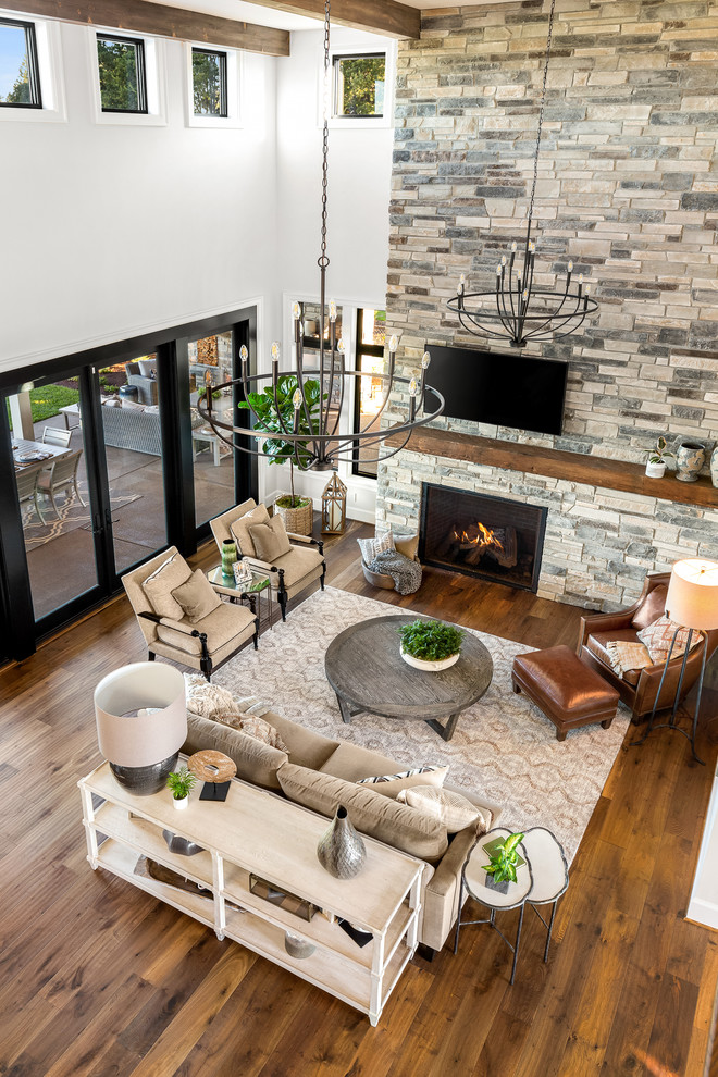 This is an example of an expansive country open concept living room in Portland with white walls, medium hardwood floors, a standard fireplace, a stone fireplace surround and a wall-mounted tv.