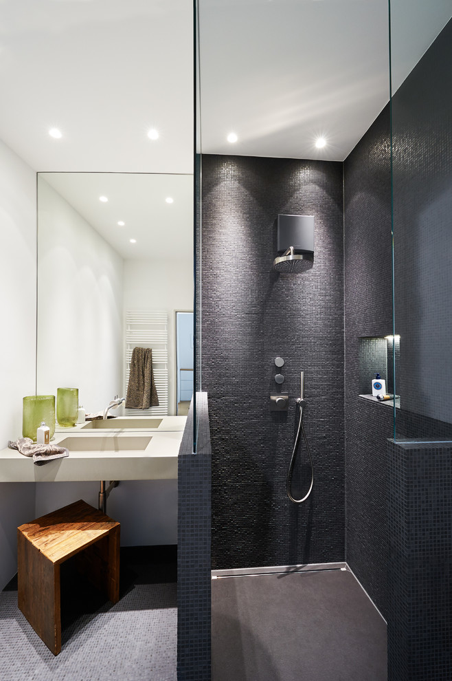 Photo of a small contemporary 3/4 bathroom in Other with a curbless shower, a two-piece toilet, black tile, mosaic tile, black walls, mosaic tile floors, an integrated sink and concrete benchtops.