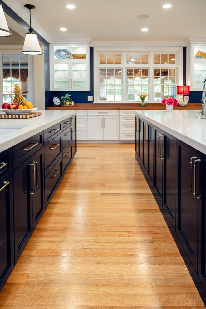 Huge transitional u-shaped brown floor kitchen photo with a farmhouse sink, shaker cabinets, quartz countertops, white backsplash, quartz backsplash, stainless steel appliances, two islands and white countertops