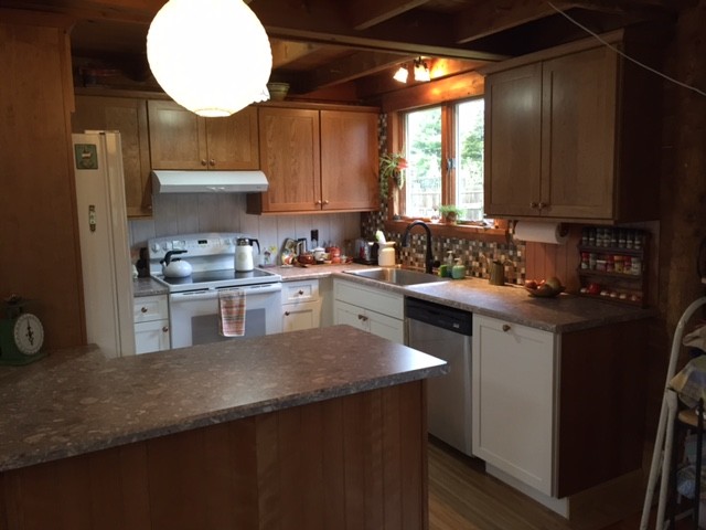 Photo of a small country u-shaped eat-in kitchen in Boston with a drop-in sink, shaker cabinets, medium wood cabinets, laminate benchtops, multi-coloured splashback, white appliances, vinyl floors and a peninsula.