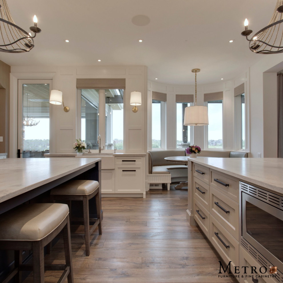 Example of a transitional u-shaped brown floor kitchen design in Calgary with a farmhouse sink, shaker cabinets, white cabinets, marble countertops, stainless steel appliances, two islands and white countertops