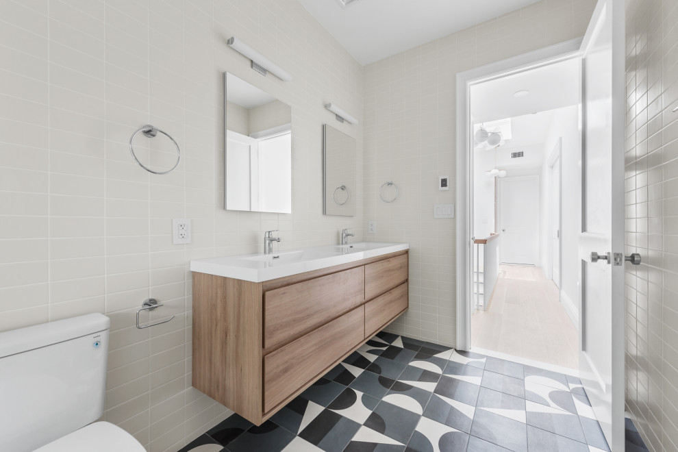 This is an example of a mid-sized transitional bathroom in New York with furniture-like cabinets, brown cabinets, a drop-in tub, an alcove shower, a one-piece toilet, gray tile, ceramic tile, beige walls, ceramic floors, a drop-in sink, marble benchtops, blue floor, a hinged shower door, white benchtops, a double vanity and a freestanding vanity.