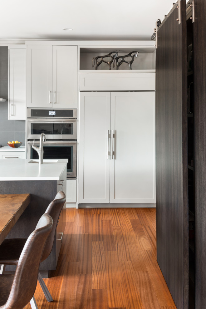 Example of a mid-sized minimalist medium tone wood floor and brown floor kitchen design with beaded inset cabinets, white cabinets and an island