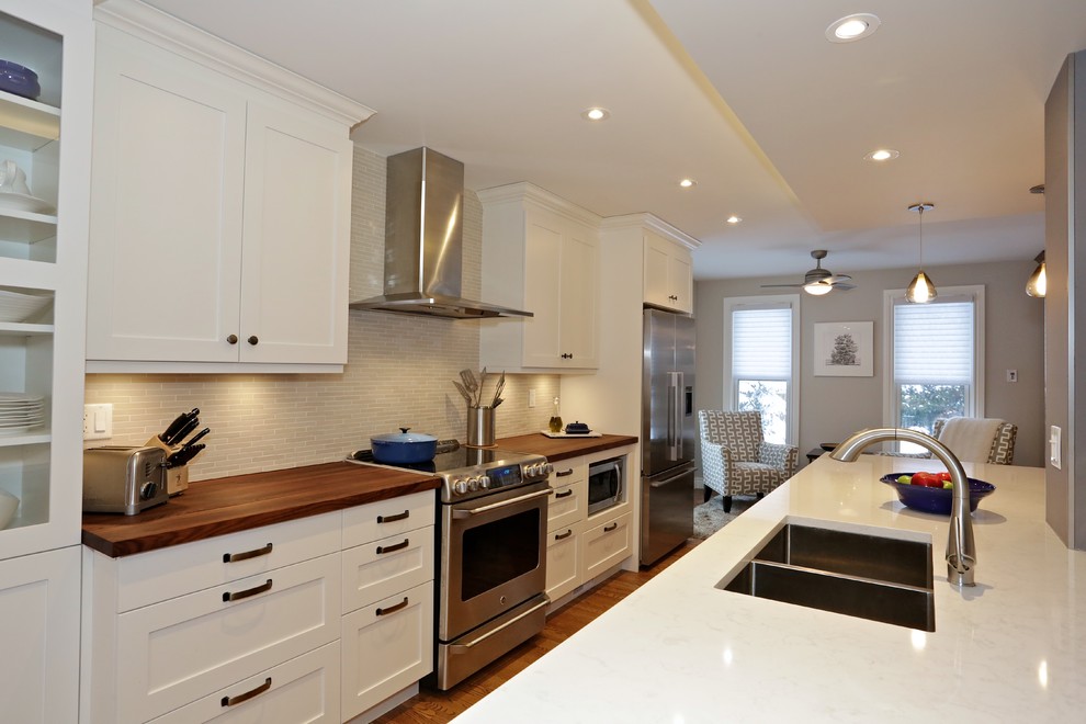 Inspiration for a transitional medium tone wood floor kitchen remodel in Ottawa with a double-bowl sink, shaker cabinets, white cabinets, quartzite countertops, beige backsplash, porcelain backsplash, stainless steel appliances and an island