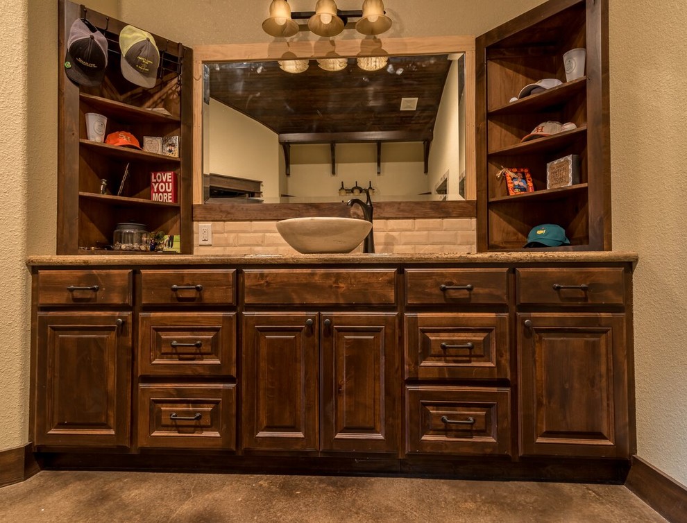 Mid-sized traditional 3/4 bathroom in Austin with raised-panel cabinets, medium wood cabinets, beige tile, stone tile, beige walls, concrete floors, a vessel sink, granite benchtops and a freestanding tub.
