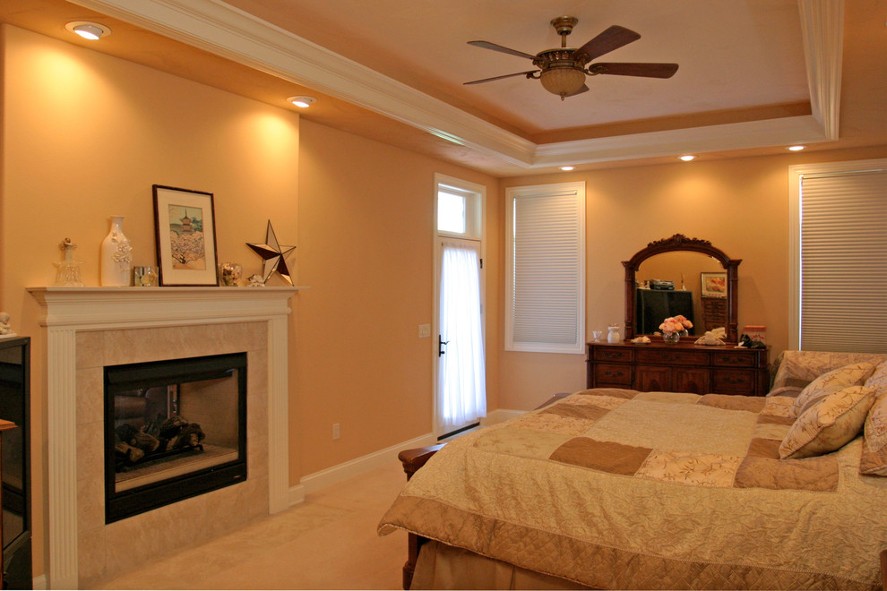 Photo of a mid-sized traditional master bedroom in Milwaukee with beige walls, carpet, a two-sided fireplace and a stone fireplace surround.