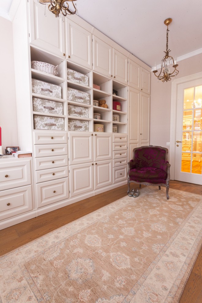 Traditional gender-neutral dressing room in Moscow with raised-panel cabinets, white cabinets, medium hardwood floors and brown floor.