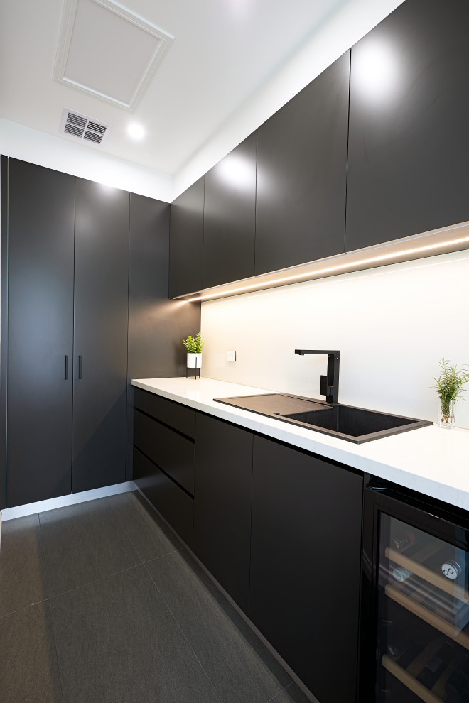 This is an example of a modern u-shaped separate kitchen in Melbourne with a drop-in sink, flat-panel cabinets, black cabinets, quartz benchtops, white splashback, glass sheet splashback, black appliances, porcelain floors, with island, grey floor and white benchtop.