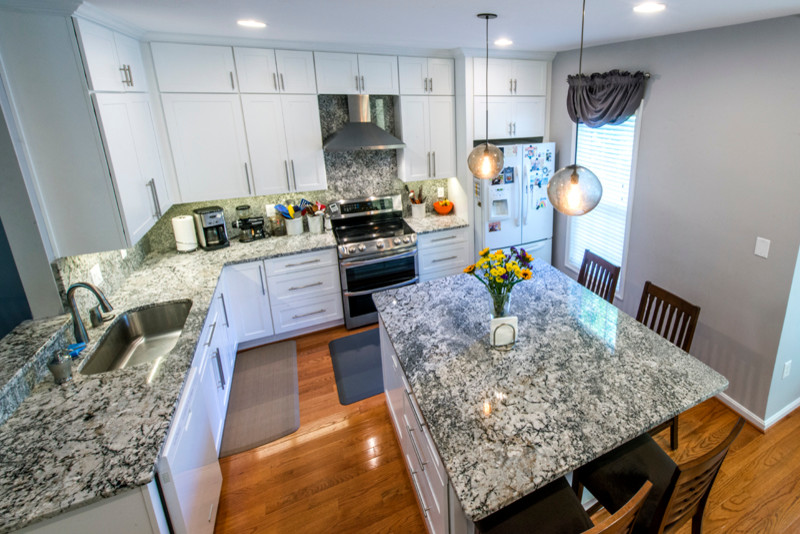 Mid-sized l-shaped kitchen in DC Metro with an undermount sink, white cabinets, granite benchtops, grey splashback, stainless steel appliances, light hardwood floors and with island.