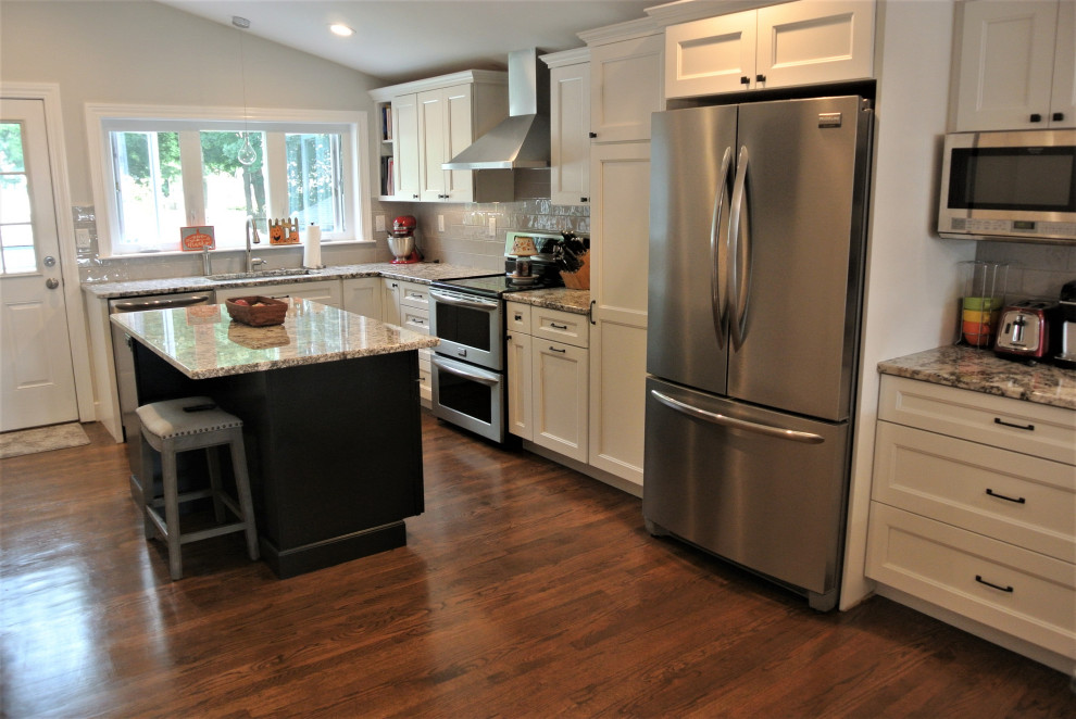Inspiration for a transitional l-shaped medium tone wood floor and brown floor eat-in kitchen remodel in Boston with an undermount sink, shaker cabinets, white cabinets, granite countertops, beige backsplash, subway tile backsplash, stainless steel appliances, an island and beige countertops