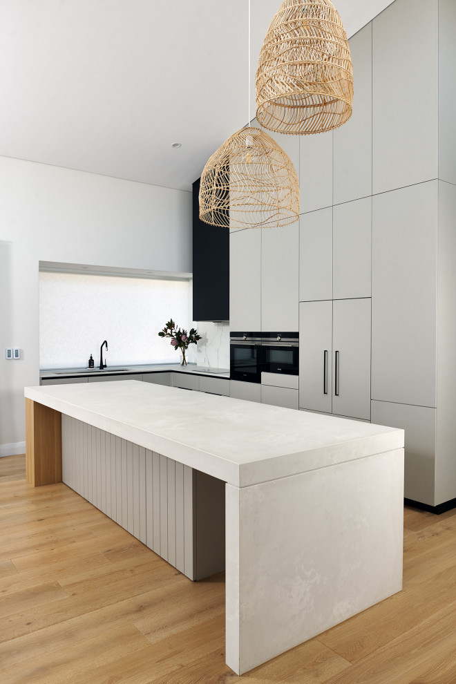 Inspiration for a large scandinavian l-shaped kitchen/diner in Perth with a double-bowl sink, flat-panel cabinets, grey cabinets, engineered stone countertops, white splashback, porcelain splashback, black appliances, light hardwood flooring, an island, beige floors, white worktops and a vaulted ceiling.