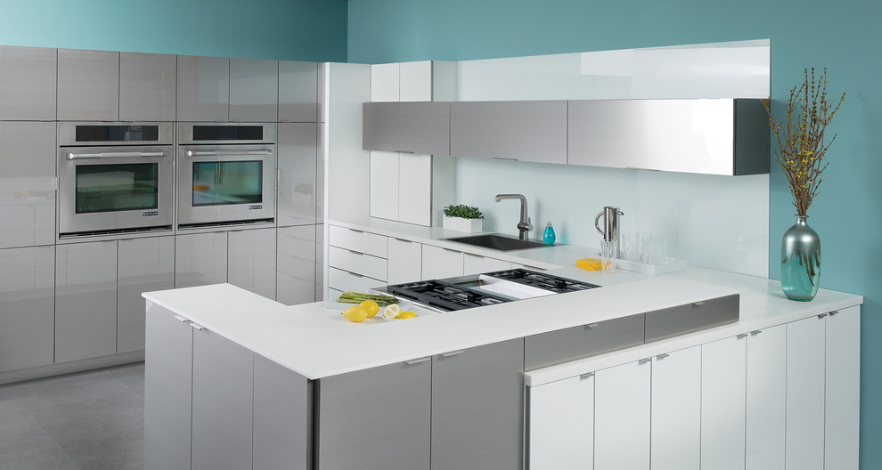 Contemporary u-shaped kitchen in Chicago with a drop-in sink, flat-panel cabinets, white cabinets, white splashback, glass sheet splashback, stainless steel appliances and a peninsula.