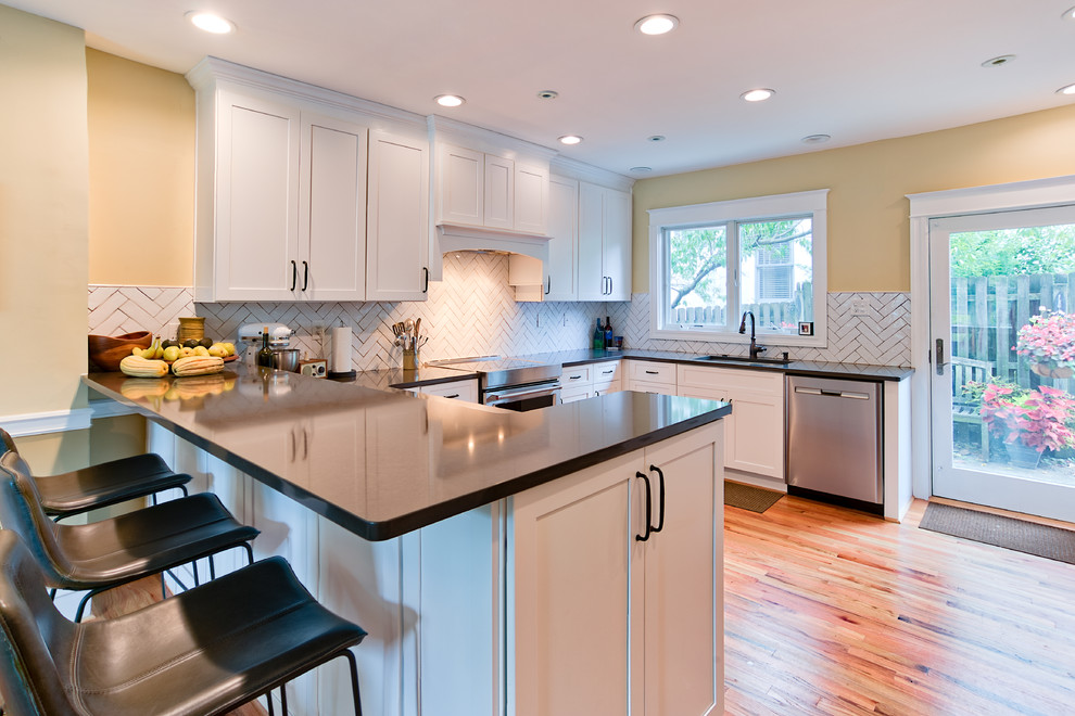 This is an example of a mid-sized transitional u-shaped eat-in kitchen in Philadelphia with shaker cabinets, white cabinets, glass benchtops, white splashback, subway tile splashback, light hardwood floors, a peninsula, multi-coloured floor and brown benchtop.