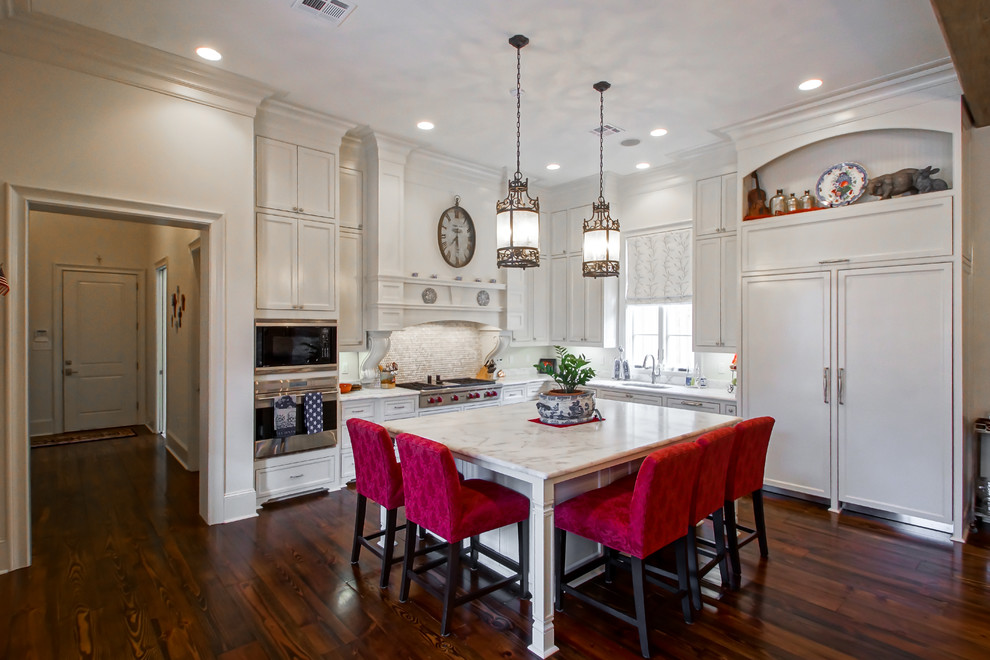 Mid-sized transitional l-shaped eat-in kitchen in New Orleans with an undermount sink, raised-panel cabinets, white cabinets, marble benchtops, white splashback, porcelain splashback, stainless steel appliances, medium hardwood floors and with island.