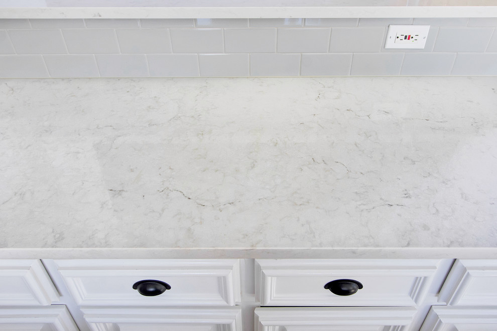 Eat-in kitchen - mid-sized transitional eat-in kitchen idea in Dallas with an undermount sink, raised-panel cabinets, white cabinets, quartz countertops, gray backsplash, ceramic backsplash, stainless steel appliances and an island
