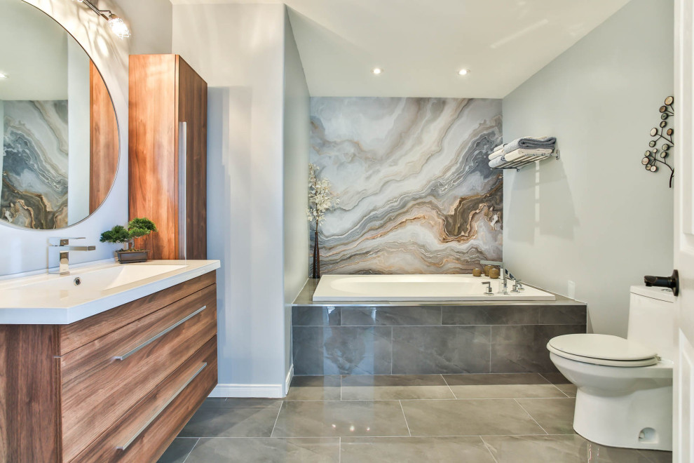This is an example of a mid-sized contemporary master bathroom in Ottawa with flat-panel cabinets, medium wood cabinets, a drop-in tub, a corner shower, a one-piece toilet, white tile, ceramic tile, grey walls, ceramic floors, an integrated sink, glass benchtops, grey floor, an open shower, white benchtops, a single vanity, a floating vanity and wallpaper.