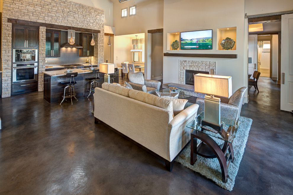 This is an example of a large contemporary open concept family room in Austin with beige walls, concrete floors, a standard fireplace, a stone fireplace surround and a wall-mounted tv.
