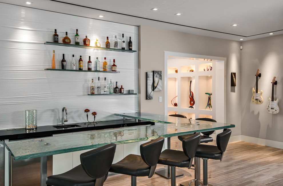 Design ideas for a large contemporary l-shaped wet bar in Miami with an undermount sink, glass benchtops, white splashback, porcelain floors and beige floor.