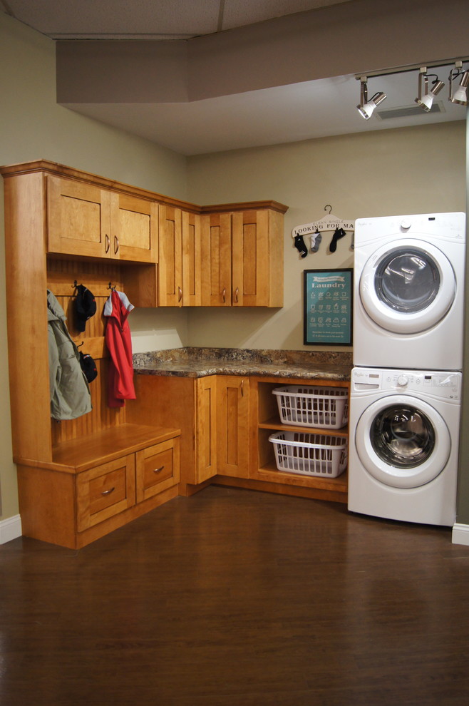 This is an example of a mid-sized traditional l-shaped utility room in Other with shaker cabinets, laminate benchtops, dark hardwood floors, a stacked washer and dryer, beige walls and medium wood cabinets.