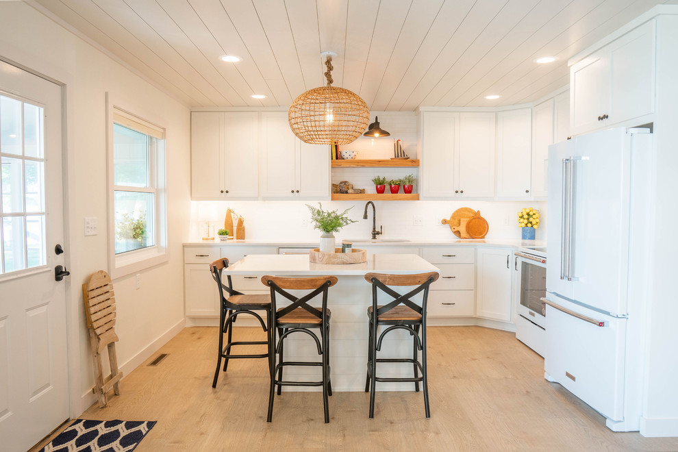 Mid-sized beach style l-shaped eat-in kitchen in Other with light hardwood floors, beige floor, an undermount sink, shaker cabinets, white cabinets, quartz benchtops, white splashback, subway tile splashback, white appliances, with island and white benchtop.