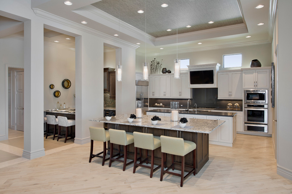 Eat-in kitchen - large transitional single-wall light wood floor eat-in kitchen idea with a drop-in sink, recessed-panel cabinets, white cabinets, granite countertops, gray backsplash, stainless steel appliances and two islands