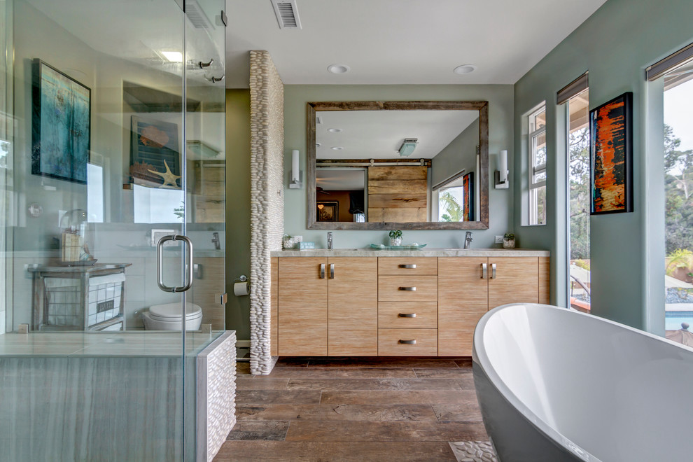 Photo of a large beach style master bathroom in San Diego with an undermount sink, flat-panel cabinets, light wood cabinets, quartzite benchtops, a freestanding tub, a curbless shower, a wall-mount toilet, brown tile, pebble tile, grey walls and porcelain floors.